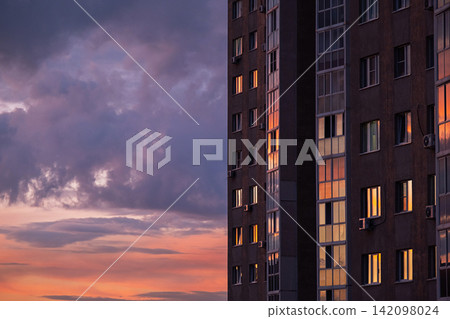 Residential apartment building with illuminated windows against dramatic sunset sky. Residential apartment building with illuminated windows against dramatic sunset sky. 142098024