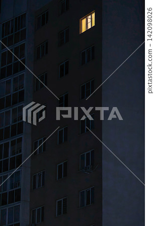 Dark apartment building facade at night with one warmly lit window. Dark apartment building facade at night with one warmly lit window. 142098026