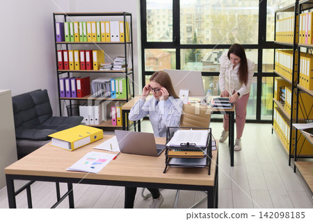 Two women organizing paperwork and computer work in bright modern office with colorful binders, documents, shelves, large windows, business routine, teamwork, productivity Two women organizing paperwork and computer work in bright modern office with colorful binders, documents, shelves, large windows, business routine, teamwork, productivity 142098185