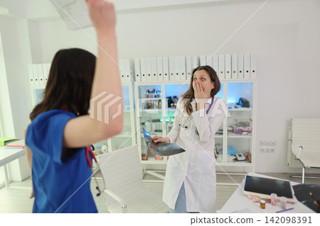 Surprised female doctor holding x ray film while patient raises hand in modern clinic office, tense consultation moment with medical files, bright interior, professional healthcare setting Surprised female doctor holding x ray film while patient raises hand in modern clinic office, tense consultation moment with medical files, bright interior, professional healthcare setting 142098391
