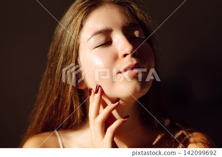 Young woman enjoying sunlight while relaxing indoors during daytime. Concept of naturalness, beauty Young woman enjoying sunlight while relaxing indoors during daytime. Concept of naturalness, beauty 142099692