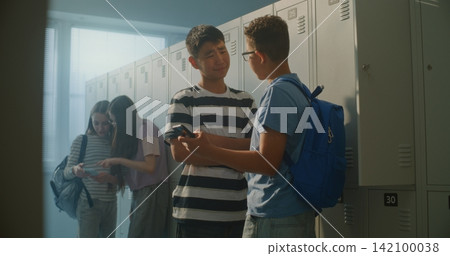 School Friends Gathers around Smartphone near Lockers, Laughing Reacting Together School Friends Gathers around Smartphone near Lockers, Laughing Reacting Together 142100038