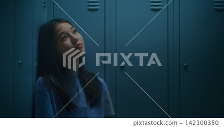 Teenage Girl Resting beside School Lockers, Gazing into Distance as Processes Emotions Teenage Girl Resting beside School Lockers, Gazing into Distance as Processes Emotions 142100350