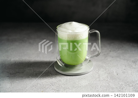 Matcha latte with frothy milk and green tea powder in glass cup. Healthy food, nutrition and antioxidant on dark background with copy space Matcha latte with frothy milk and green tea powder in glass cup. Healthy food, nutrition and antioxidant on dark background with copy space 142101109