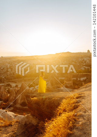 Young woman in yellow dress during sunrise watching hot air balloons in Cappadocia, Turkey Young woman in yellow dress during sunrise watching hot air balloons in Cappadocia, Turkey 142101448