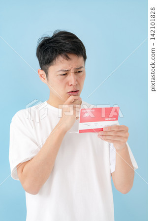 一位中年男子一邊看著存摺一邊沉思。 一位中年男子一邊看著存摺一邊沉思。 142101828