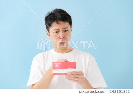 一位中年男子一邊看著存摺一邊沉思。 一位中年男子一邊看著存摺一邊沉思。 142101831