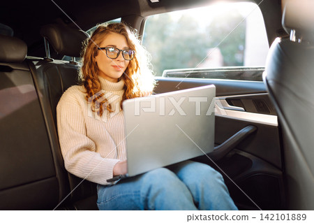 Young woman in glasses with a laptop in the back seat of a car. Freelance, business concept. Young woman in glasses with a laptop in the back seat of a car. Freelance, business concept. 142101889