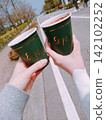 Two hands holding warm drinks outdoors 142102252
