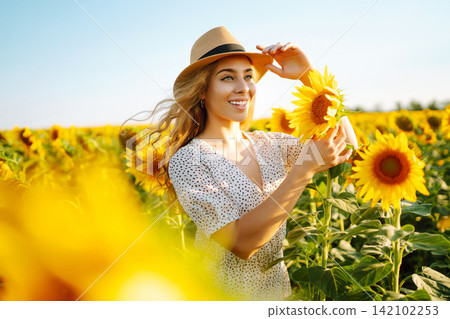 Happy woman posing in a field of sunflowers in hat. Fashion, lifestyle, travel and vacations concept Happy woman posing in a field of sunflowers in hat. Fashion, lifestyle, travel and vacations concept 142102253