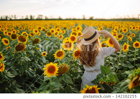 Happy woman posing in a field of sunflowers in hat. Fashion, lifestyle, travel and vacations concept Happy woman posing in a field of sunflowers in hat. Fashion, lifestyle, travel and vacations concept 142102255