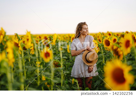 Happy woman posing in a field of sunflowers in hat. Fashion, lifestyle, travel and vacations concept Happy woman posing in a field of sunflowers in hat. Fashion, lifestyle, travel and vacations concept 142102256