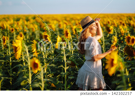 Happy woman posing in a field of sunflowers in hat. Fashion, lifestyle, travel and vacations concept Happy woman posing in a field of sunflowers in hat. Fashion, lifestyle, travel and vacations concept 142102257