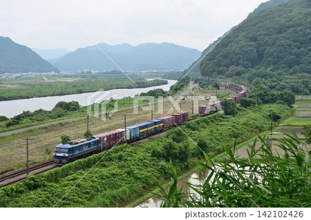 以岡山縣的大河吉井川為背景,在山陽公路上快速行駛的長長的貨運列車。 以岡山縣的大河吉井川為背景,在山陽公路上快速行駛的長長的貨運列車。 142102426