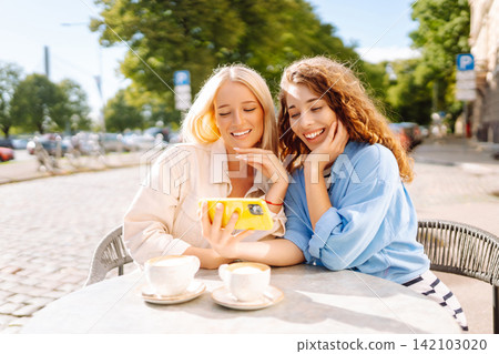 Smiling woman are sitting in a cafe, taking selfies, talking with friends. Fashion, beauty. 142103020