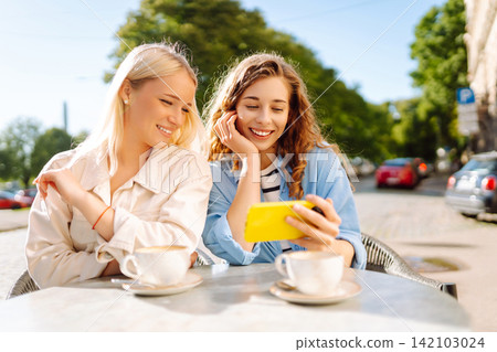 Smiling woman are sitting in a cafe, taking selfies, talking with friends. Fashion, beauty. 142103024