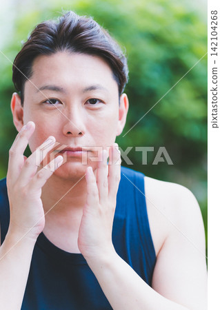 A man in his 40s uses botanical facial care outdoors, applying the product to his face with both hands. A man in his 40s uses botanical facial care outdoors, applying the product to his face with both hands. 142104268