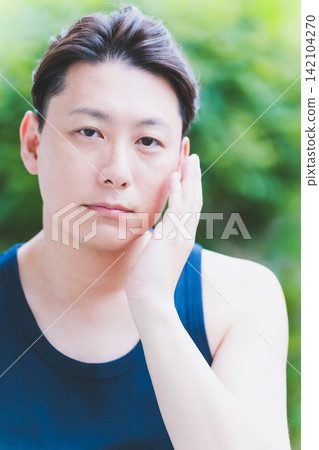 A 40-year-old man seriously applying botanical skincare to his cheek with one hand outdoors. A 40-year-old man seriously applying botanical skincare to his cheek with one hand outdoors. 142104270