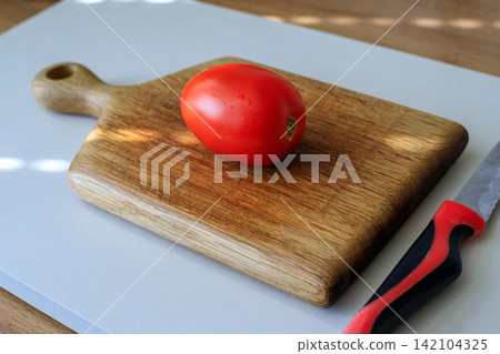 Fresh red ripe tomato and a paring knife resting on a wooden cutting board in a kitchen. Home cooking, healthy eating, and fresh ingredients Fresh red ripe tomato and a paring knife resting on a wooden cutting board in a kitchen. Home cooking, healthy eating, and fresh ingredients 142104325