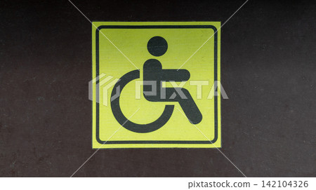 Yellow Wheelchair Accessible Symbol Sticker Mounted on Dark Surface Yellow Wheelchair Accessible Symbol Sticker Mounted on Dark Surface 142104326