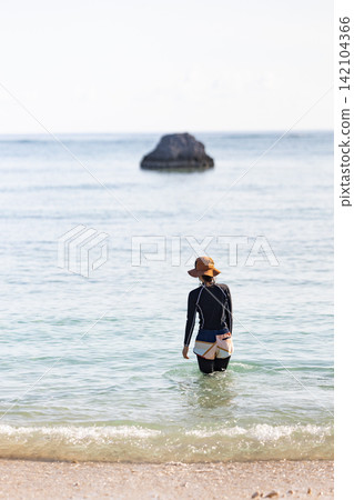 The back view of a woman walking into the calm sea on a sunny day. The back view of a woman walking into the calm sea on a sunny day. 142104366