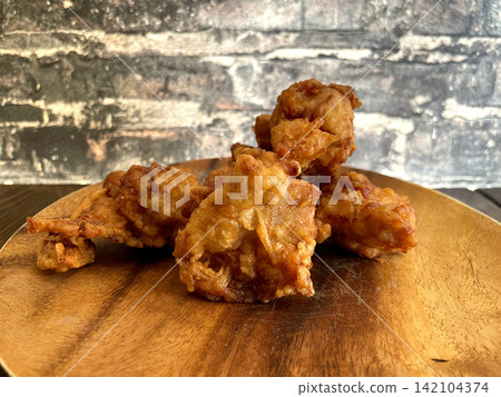 Deep-fried young chicken served on a wooden plate, crispy fried, against a brick background. Deep-fried young chicken served on a wooden plate, crispy fried, against a brick background. 142104374