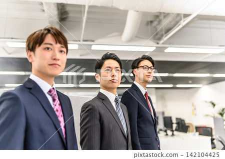 Three men looking straight ahead in an office. 142104425