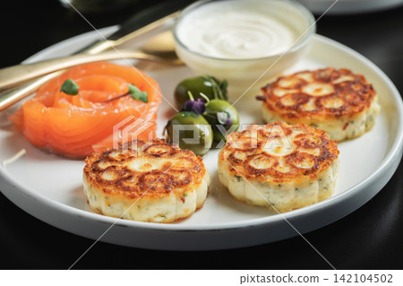 Savory Syrniki with Smoked Salmon, Olives and Sour Cream on White Plate Savory Syrniki with Smoked Salmon, Olives and Sour Cream on White Plate 142104502
