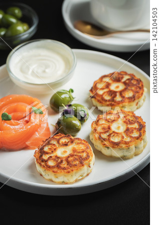 Savory Syrniki with Smoked Salmon, Olives and Sour Cream on White Plate Savory Syrniki with Smoked Salmon, Olives and Sour Cream on White Plate 142104503