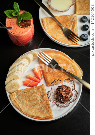 A plate of crepes filled with chocolate spread and topped with banana slices and mint A plate of crepes filled with chocolate spread and topped with banana slices and mint 142104508