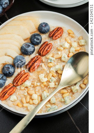 Oatmeal. Bowl of oatmeal porridge with blackberry, bananas and chia seeds on gray concrete old table background. Top view in flat lay style. Natural ingredients. Hot healthy breakfast and diet food 142104531