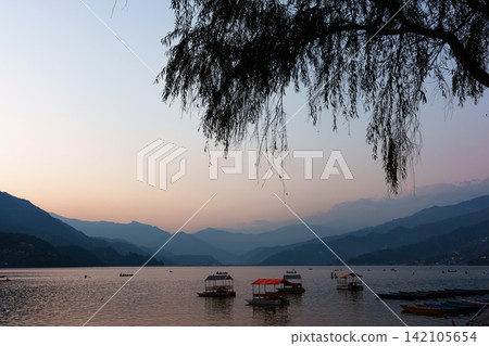 尼泊爾博卡拉費瓦湖日落:湖面上漂浮著船隻,周圍是美麗的山脈景色。 尼泊爾博卡拉費瓦湖日落:湖面上漂浮著船隻,周圍是美麗的山脈景色。 142105654