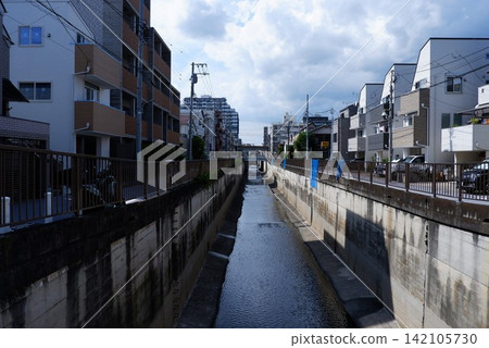 A cityscape featuring concrete waterways flowing through a residential area and power lines stretching across the streets. A cityscape featuring concrete waterways flowing through a residential area and power lines stretching across the streets. 142105730