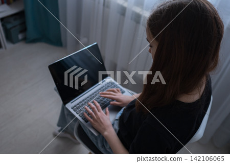 Young woman sitting with a laptop, focusing on the screen and typing on the keyboard, reflecting modern remote work, online learning, and digital communication trends 142106065
