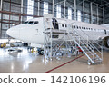 White passenger aircraft in the aviation hangar. Jet plane under maintenance. Checking mechanical systems for flight operations 142106196