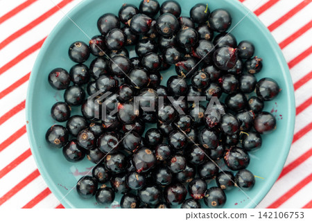Black currants in a blue bowl on red and white striped cloth 142106753