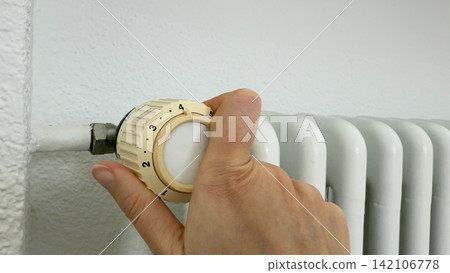 Close up on hand turning radiator thermostat knob precise temperature control for efficient home heating maintenance renovation task 142106778