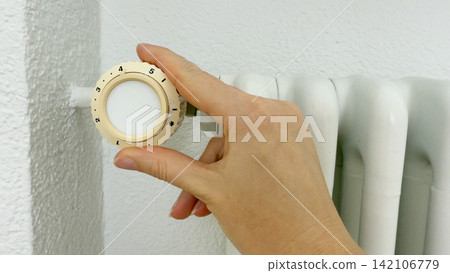 Hand setting heating thermostat on white radiator home improvement step for better climate control warm comfort energy efficiency maintenance Hand setting heating thermostat on white radiator home improvement step for better climate control warm comfort energy efficiency maintenance 142106779