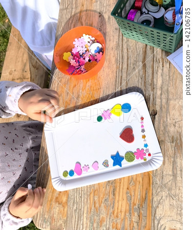 Children's hands create a photo frame, decorating it with glitter and stickers. Children's hands create a photo frame, decorating it with glitter and stickers. 142106785