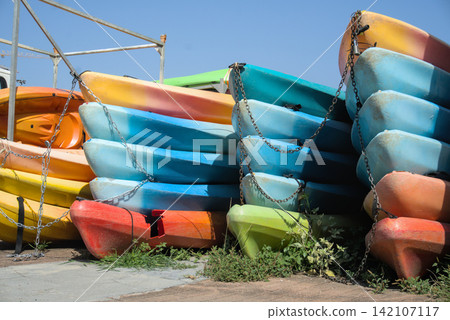 Stacked kayaks in orange, yellow and blue against a clear blue sky Stacked kayaks in orange, yellow and blue against a clear blue sky 142107117