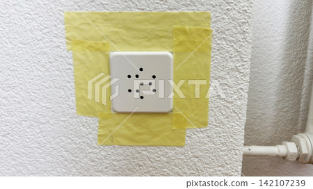 Electrical socket fully masked with yellow painter tape before home renovation safe protection for painting Electrical socket fully masked with yellow painter tape before home renovation safe protection for painting 142107239