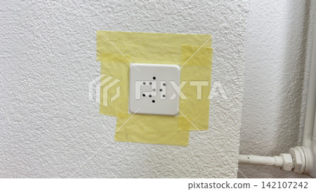 Electrical socket covered with masking tape protection before painting home renovation stage preparation for interior repair safety wall edge detail  142107242