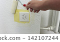 Painting wall around masked electrical socket with small roller during home renovation process careful edge work safety preparation and interior 142107244