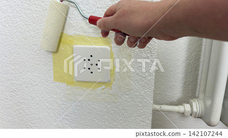 Painting wall around masked electrical socket with small roller during home renovation process careful edge work safety preparation and interior Painting wall around masked electrical socket with small roller during home renovation process careful edge work safety preparation and interior 142107244