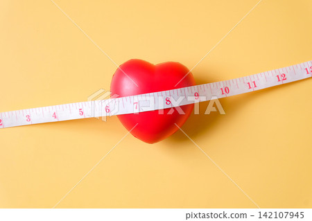 A measuring tape with Red heart ball on color background. A measuring tape with Red heart ball on color background. 142107945