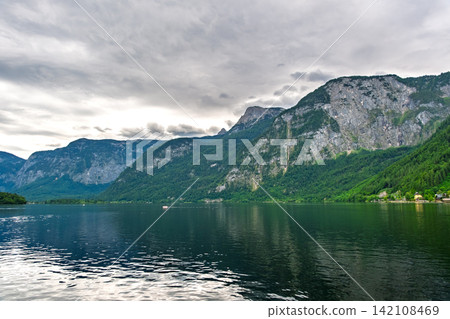 Hallstatt, Austria. The tranquil Hallstatt Lake reflects the cloudy sky and the majestic Alps. Hallstatt, Austria. The tranquil Hallstatt Lake reflects the cloudy sky and the majestic Alps. 142108469