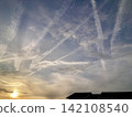 Contrails and fantastical clouds spread across the twilight sky. 142108540