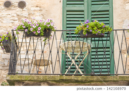 Petunia flowers pot on Italian Balcony and Window Shutters in Italy. Old cozy house Petunia flowers pot on Italian Balcony and Window Shutters in Italy. Old cozy house 142108970