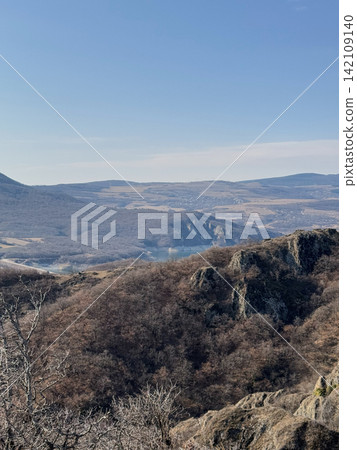 Mountain valley with visible water body and bare hills under clear sky. 142109140