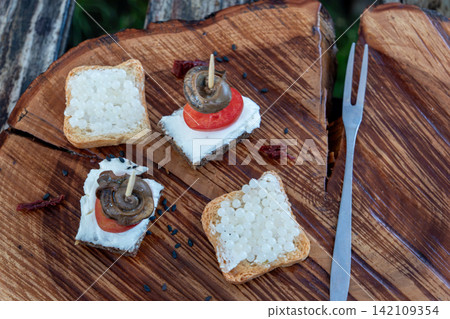 Exquisite restaurant catering snacks feature cooked mollusk flesh on bread slices with white round eggs topping served outdoors near metal fork during luxury dining. Exquisite restaurant catering snacks feature cooked mollusk flesh on bread slices with white round eggs topping served outdoors near metal fork during luxury dining. 142109354
